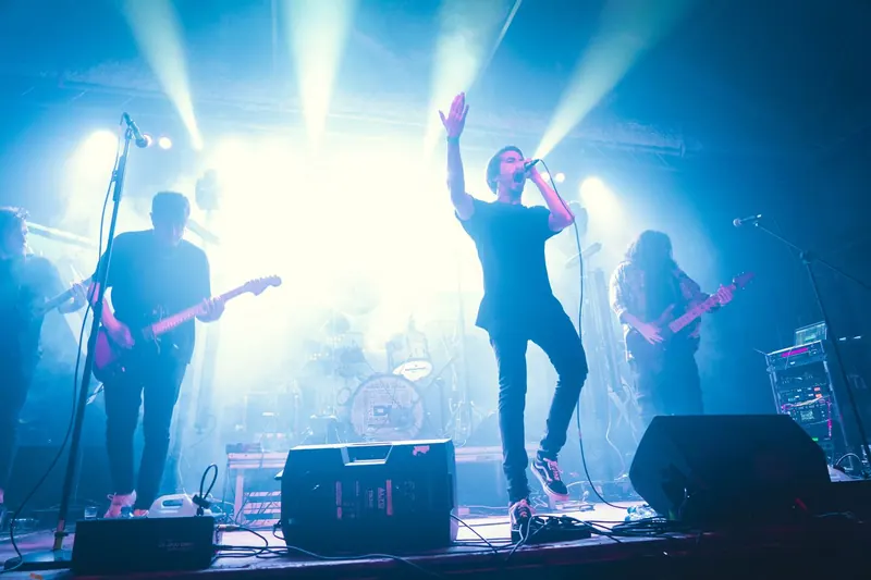 The singer mid-step with one arm up, backlit by stage lights, guitarists on both sides