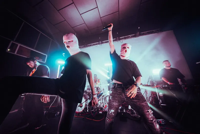 Two vocalists in balaclavas at the edge of the stage, one with the mic raised