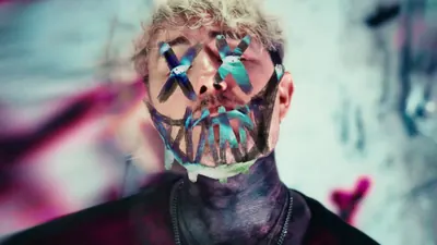 Video still: close-up of a face painted with teal X eyes and a stitched grin
