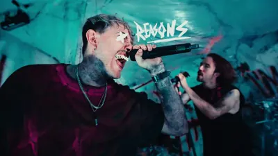 Video still: the vocalist screaming into the mic, teal light and pink paint